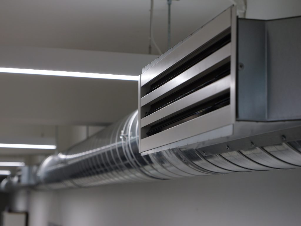 Close-up of a modern office air conditioning duct with a metal air vent diffuser attached to a suspended ceiling system.